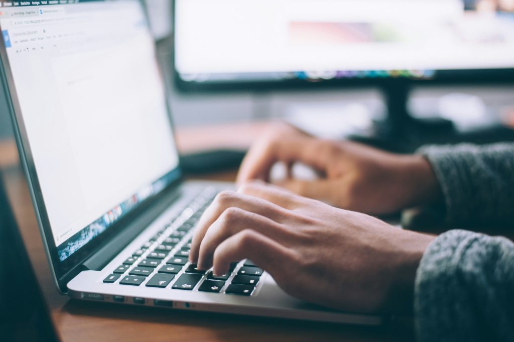 Employee typing on laptop using both hands. Monitor screen in background