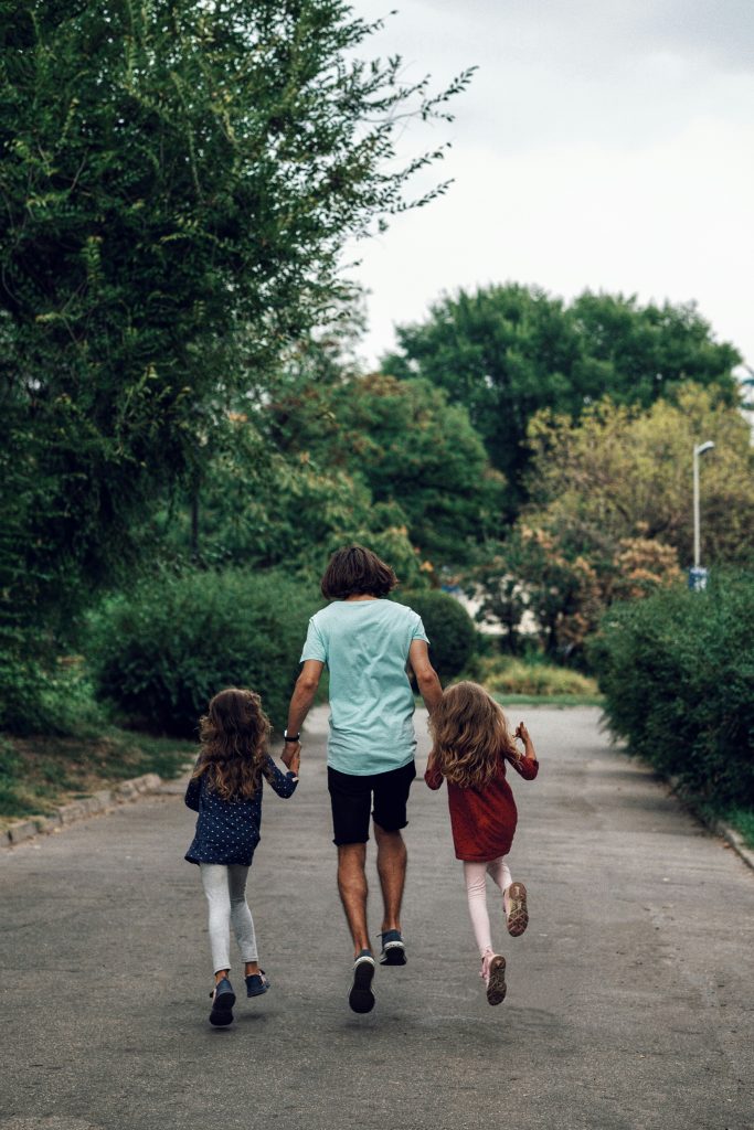 Father and two children happily skipping down path